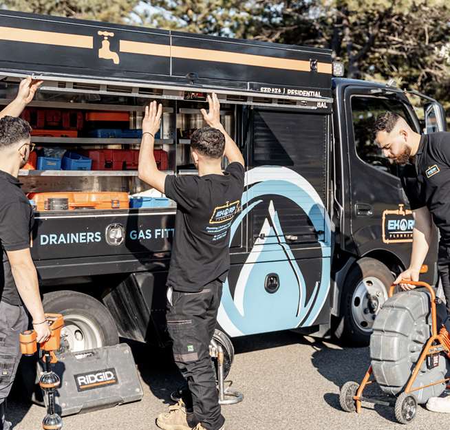 Plumbers preparing drain inspection equipment beside their service truck