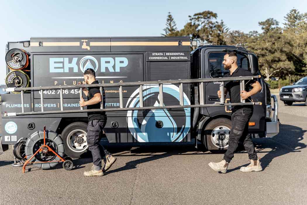 Two plumbers carrying a ladder beside their service truck